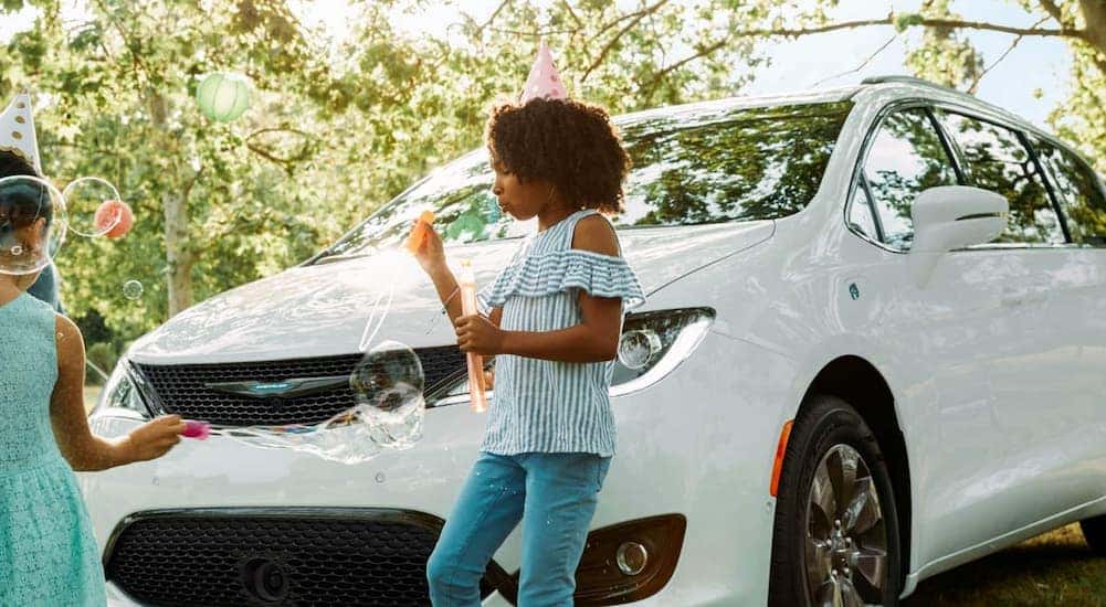 Two kids are playing in front of a white 2020 Chrysler Pacifica.