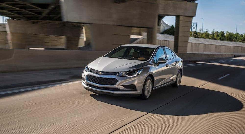 A popular used car for sale around Lexington, KY, a silver 2017 Chevy Cruze, is shown driving under a bridge.