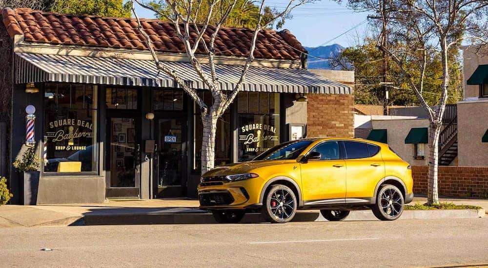 A gold 2024 Dodge Hornet R/T is shown parked outside of a barber shop.