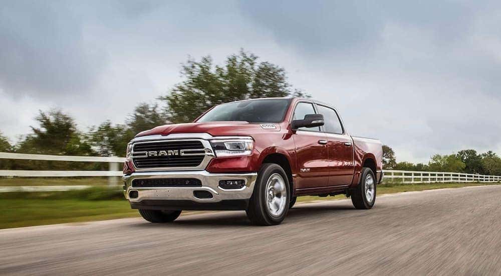 A red 2020 Ram 1500 is driving past a white fence and field after leaving a Ram dealer near Lexington, KY.