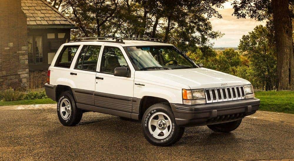 A white 1995 used Jeep Grand Cherokee is parked angled right with a cabin and forest in the background.