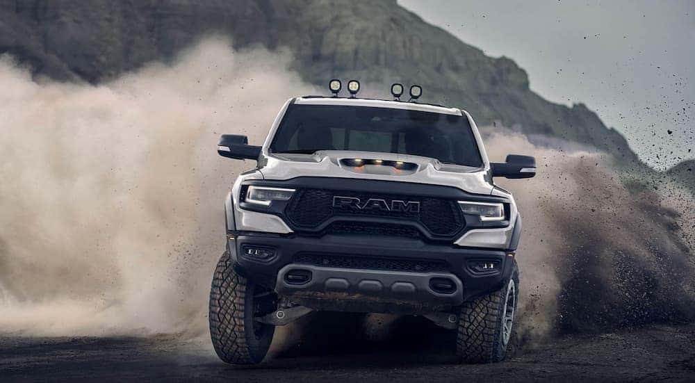 A silver 2021 Ram 1500 TRX, one of the new Ram trucks, is kicking up sand while off-roading in front of a hill.