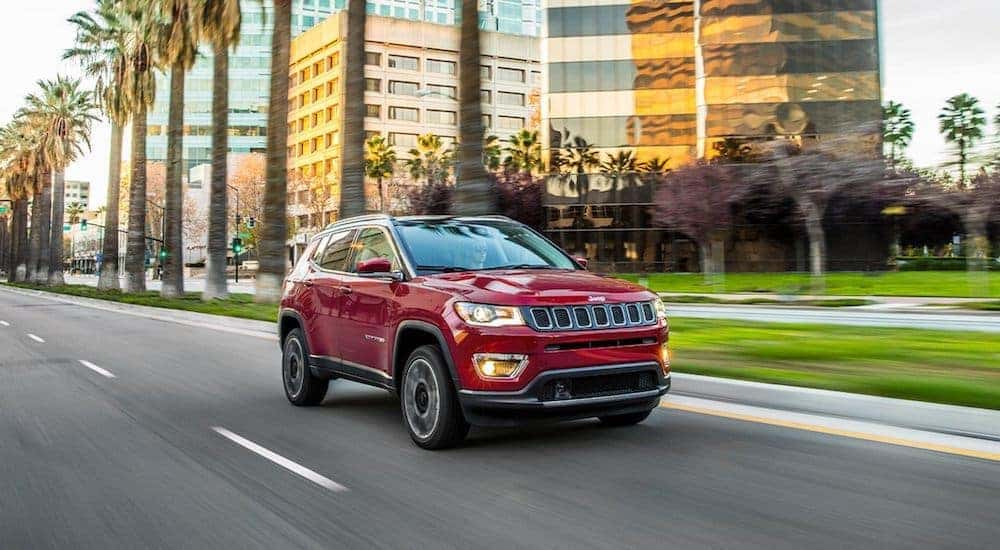 A maroon 2020 used Jeep Compass is shown driving past blurred buildings.