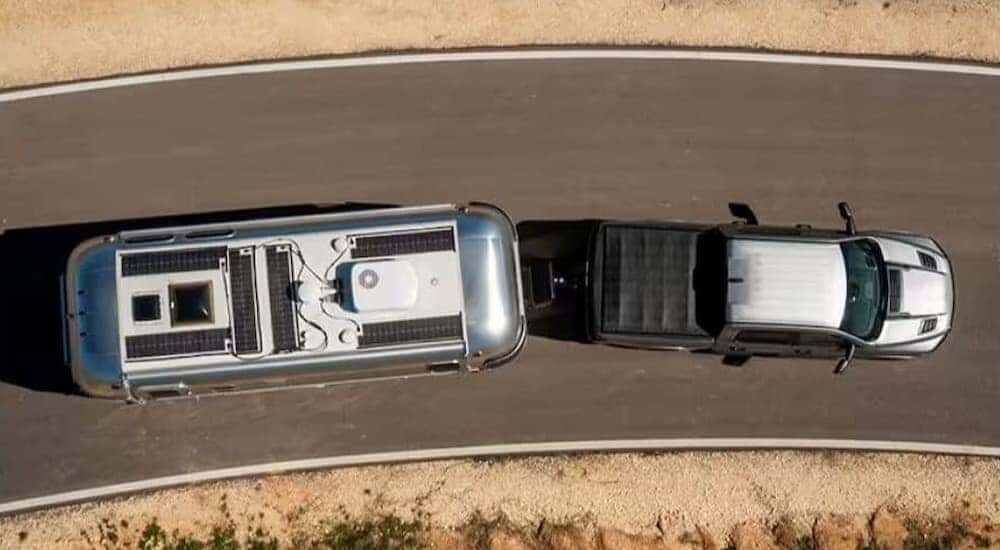 A bird's eye view of a white 2025 Ram 1500 with a bed cover towing a trailer.