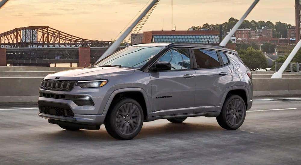 A grey 2022 Jeep Compass is shown from the side driving over a bridge.