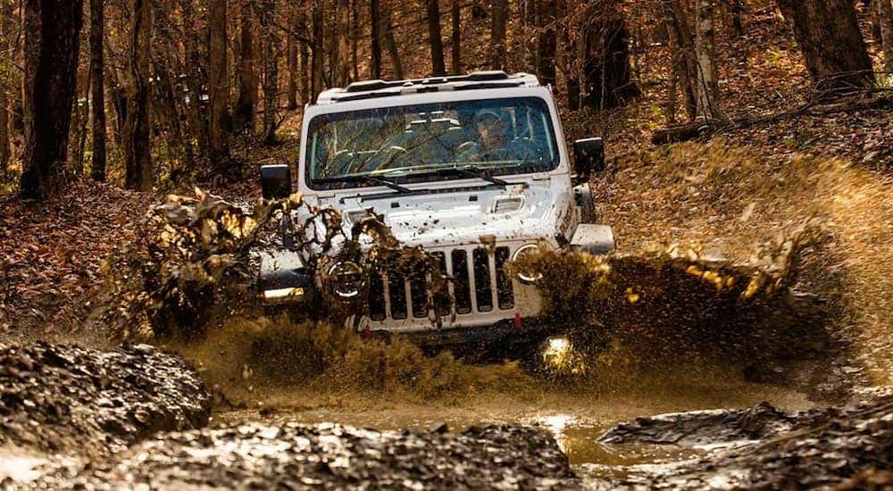 A silver 2020 used Jeep Wrangler Rubicon is shown from the front with no roof driving through the mud.