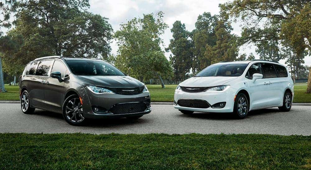 A grey and a white 2020 Chrysler Pacifica are parked in front of trees.