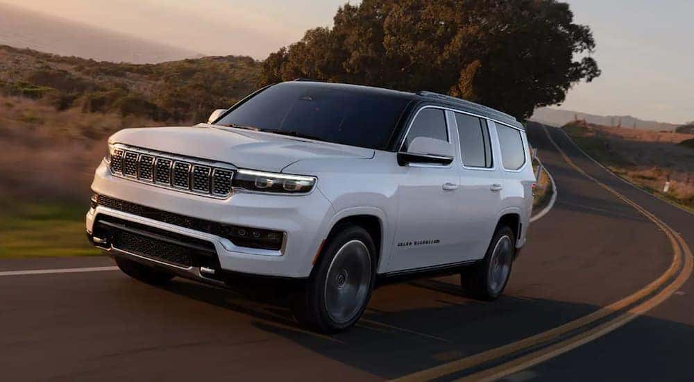 A white 2022 Grand Wagoneer is shown driving on a two lane road at sunset.