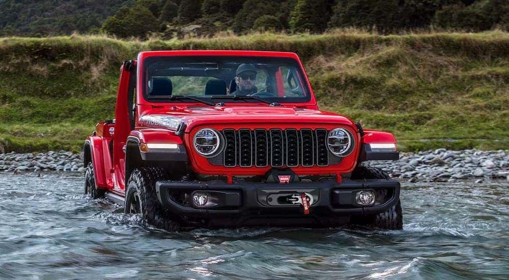 The most popular Jeep Wrangler for sale, a red 2024 Jeep Wrangler Rubicon, is shown fording a river.