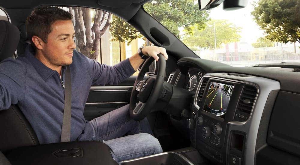 A man is shown using the backup camera while test driving a used 2022 Ram 1500 for sale.