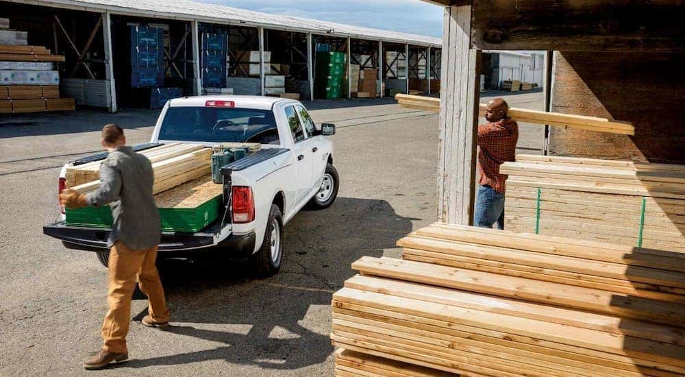 A white 2018 Ram 1500 is being used to move wooden boards at a lumber yard.