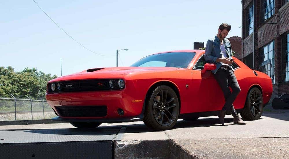 An orange 2021 Dodge Challenger is shown from the side with a man leaning against it.