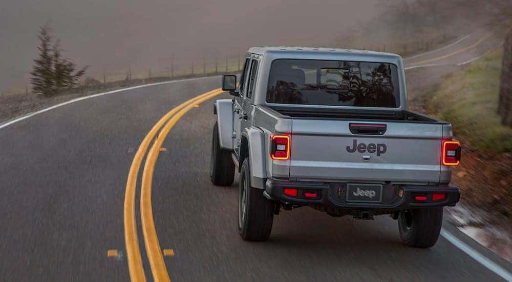 A silver 2020 used Jeep Gladiator Sport Overland is shown from behind driving down a twisty road in the fog.