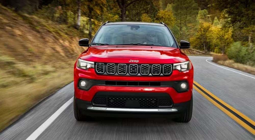 A red 2024 Jeep Compass for sale is shown driving on a highway.