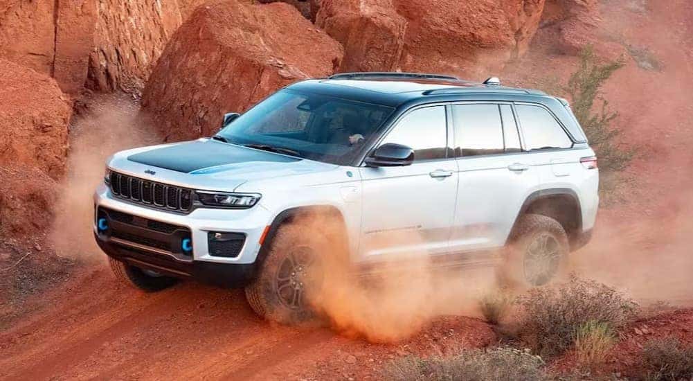 A popular Jeep Grand Cherokee for sale, a white 2024 Jeep Grand Cherokee 4xe, is shown driving off-road.