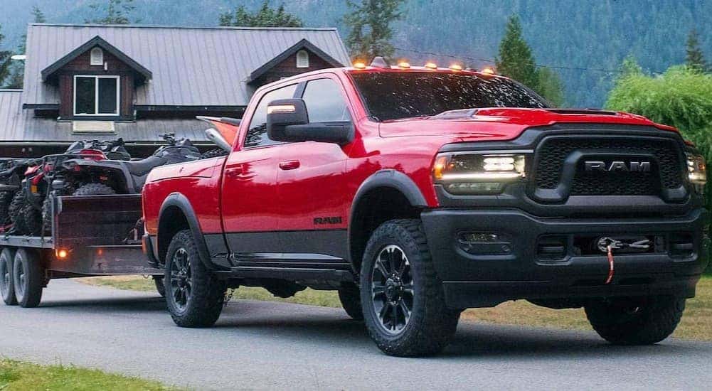 A red 2023 Ram 2500 Rebel is shown towing a trailer near a house.