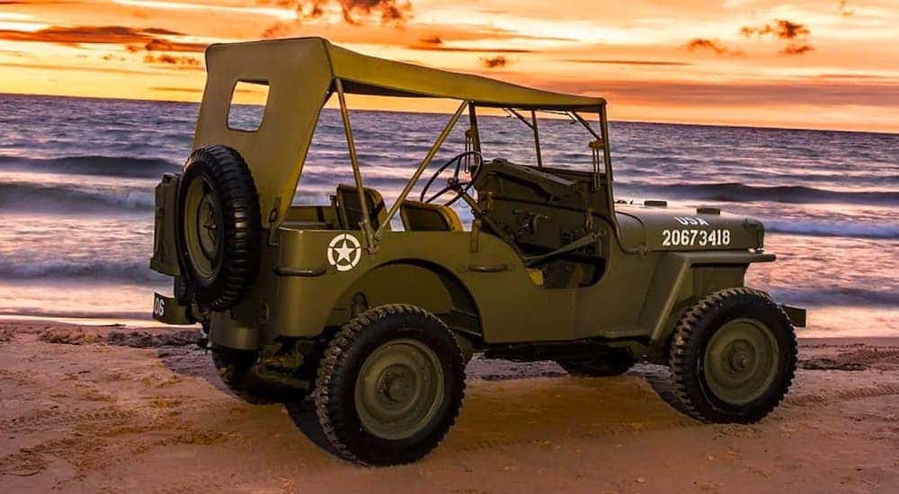 A green 1942 Jeep Willys MB is shown from the rear at an angle on an ocean shore.