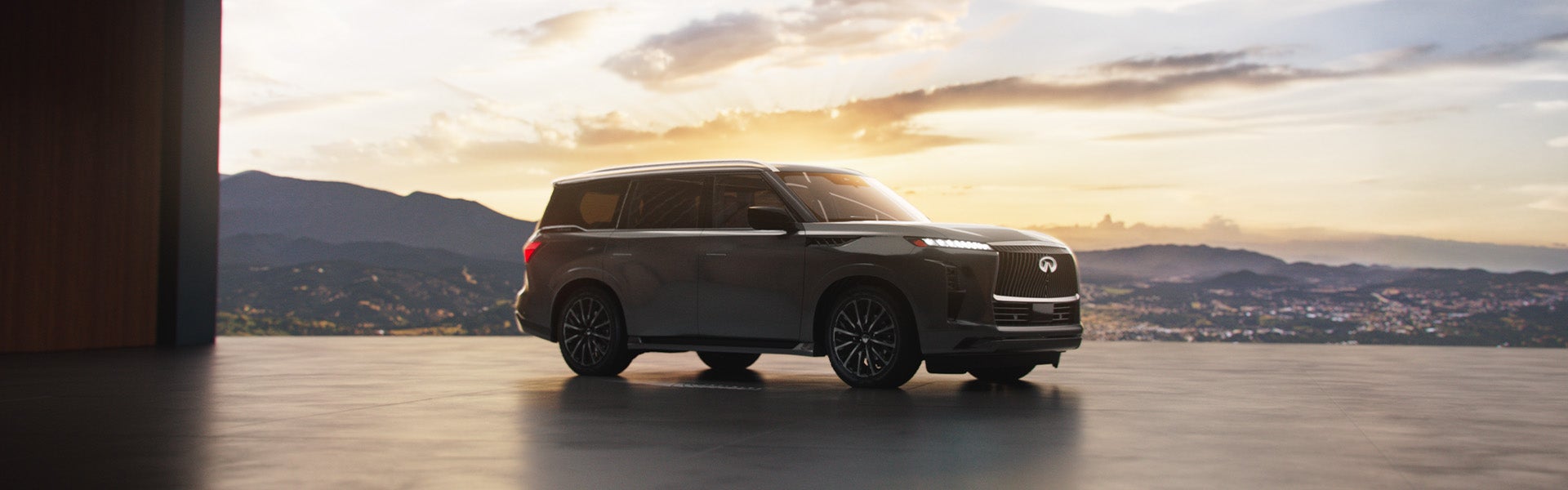 2025 Infiniti QX80 luxury SUV parked indoors with a sunset mountain backdrop.