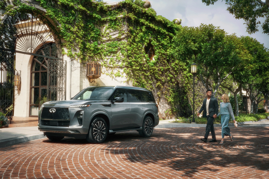couple approaching an Infiniti QX80 parked in front of a building