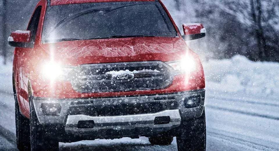 red Ford F-150 driving in snowstorm with headlights on