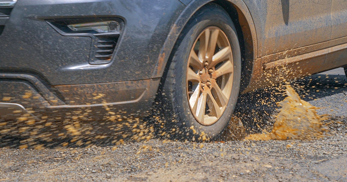 Ford SUV tire kicking up gravel and mud on rough terrain, showcasing off-road capability and rugged performance