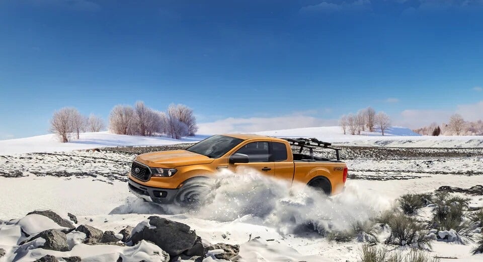 orange Ford F-150 driving through snowdrift on sunny winter dat