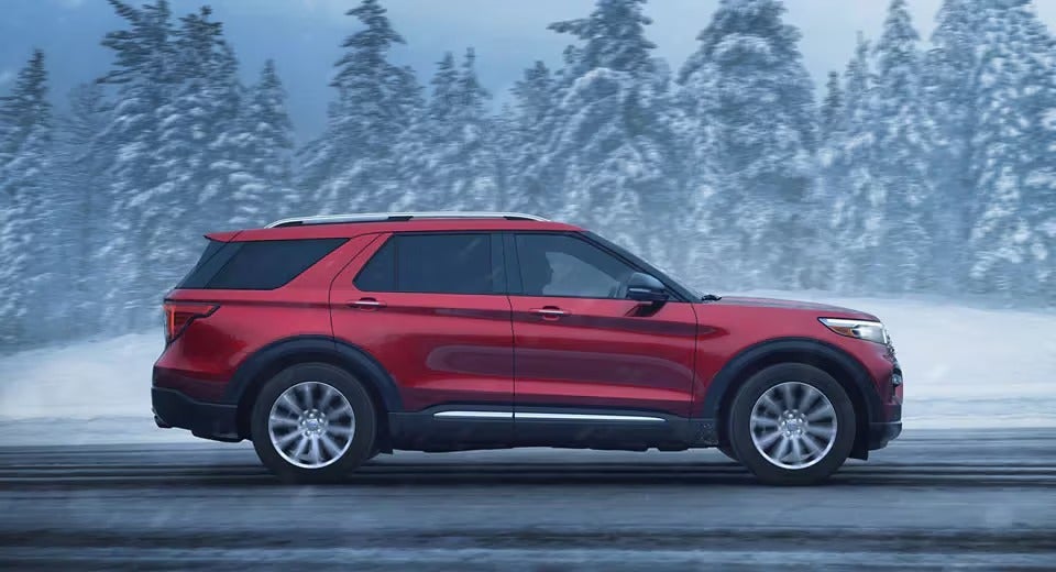 side view of a red Ford Explorer driving on a snowy road in wintertime