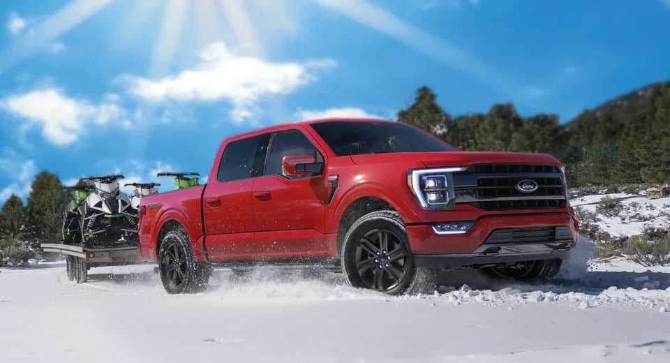 red Ford F-150 pulling two snowmobiles on a trailer in the winter