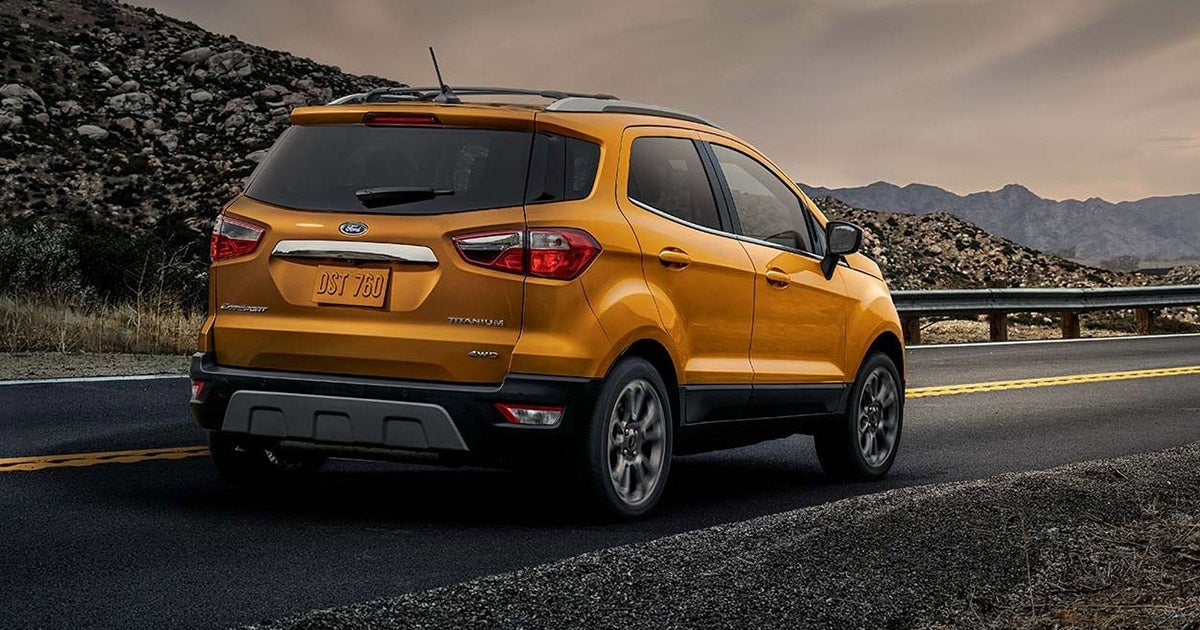 Ford EcoSport Titanium in vibrant yellow, driving on mountain road with rocky terrain and sunset backdrop