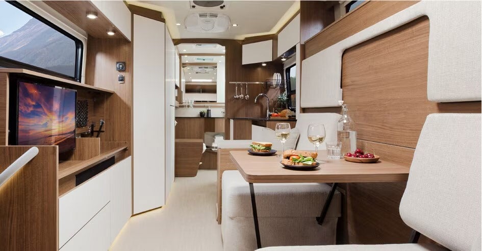 Interior of modern Ford camper van with wooden finishes, dining area, meals prepared, white and wood color scheme, compact living space design