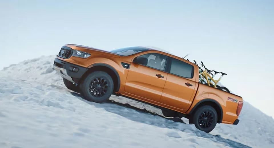 orange Ford F-150 driving up an offroad snowy hill in winter time