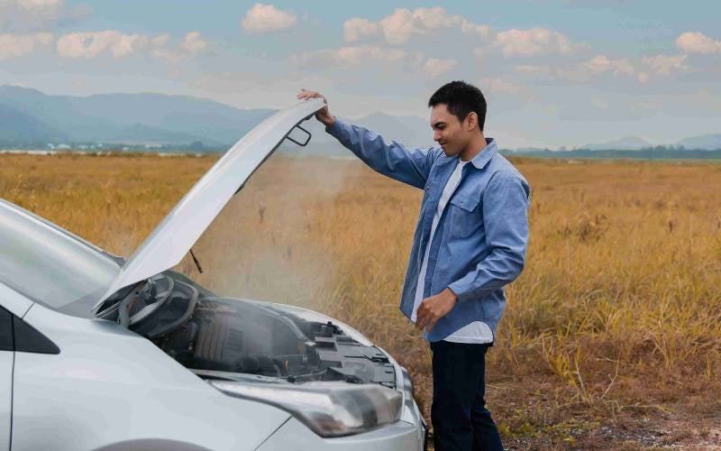 guy looking under hood of his car on a fall day