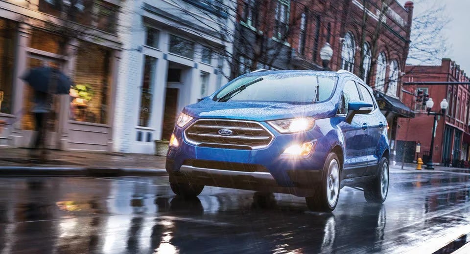 compact Ford driving in a small downtown in the rainstorm with headlights on