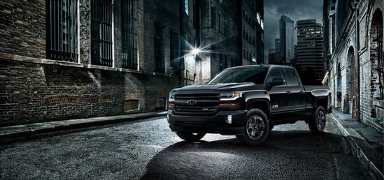 black Chevrolet parked in front of a brick building at night
