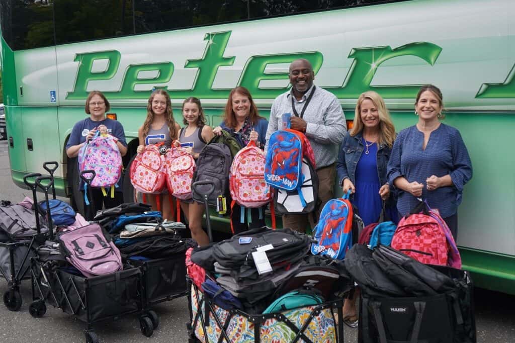 A group of people with backpacks stands in front of a bus