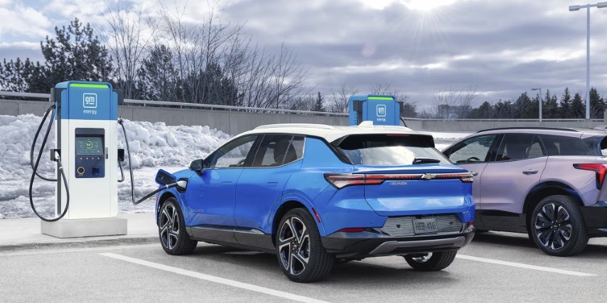 Blue Chevrolet electric SUV charging at a GM Energy station in a snowy parking lot next to a second EV.