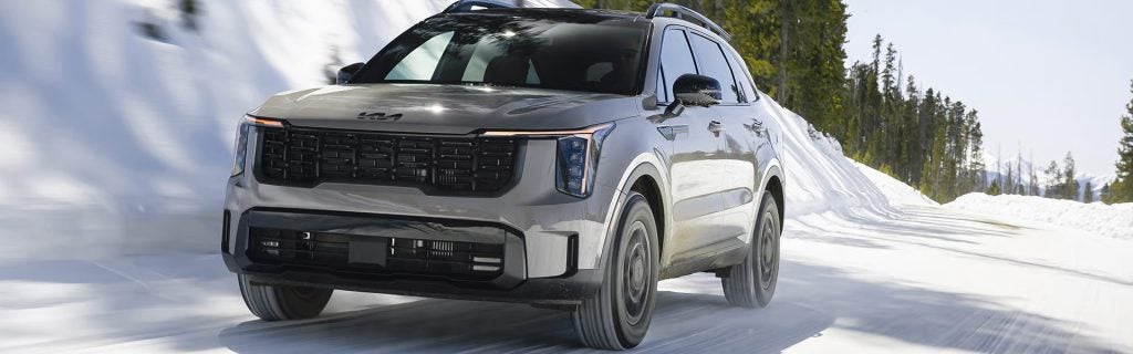 A gray SUV driving on a snowy road, with trees and snowbanks in the background.