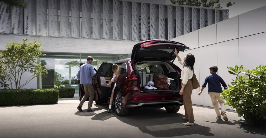 Family loading luggage into a 2026 Mazda CX-90 SUV parked outside a modern home, showcasing spacious cargo capacity and everyday versatility.