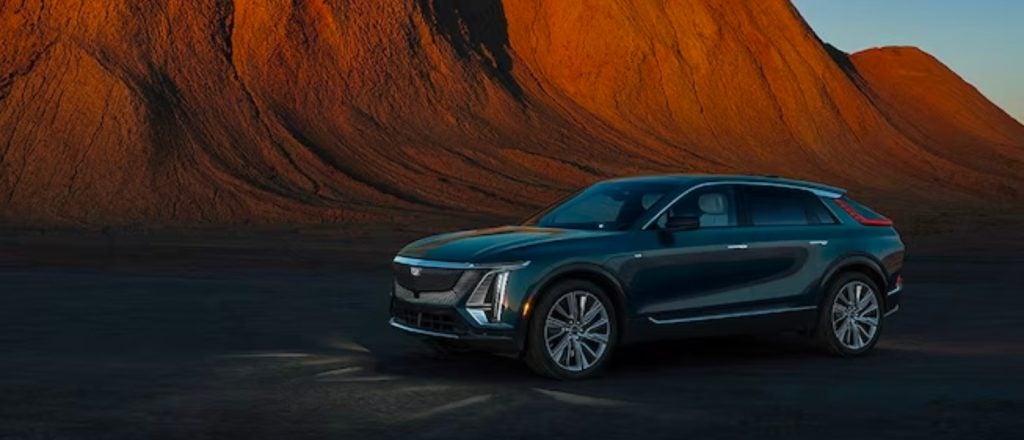 green cadillac lyriq parked in front of red hills at sunset
