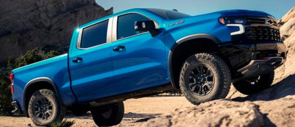 blue Chevrolet Silverado driving up a rocky hill in the desert