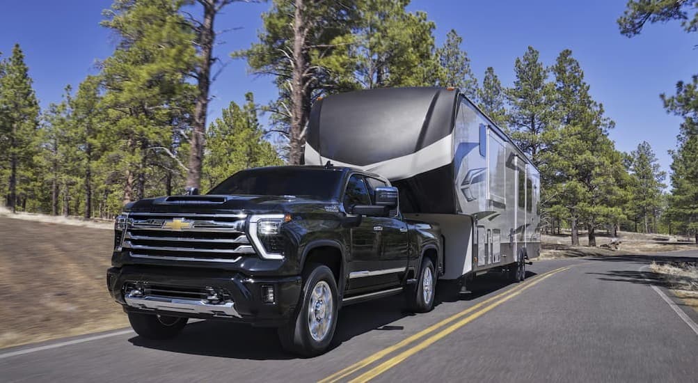 A black 2026 Chevy Silverado 2500 towing a trailer to view heavy duty trucks for sale.