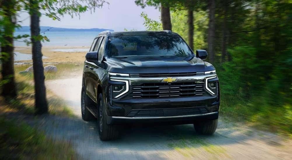 A blue 2025 Chevy Suburban is shown driving near a lake.