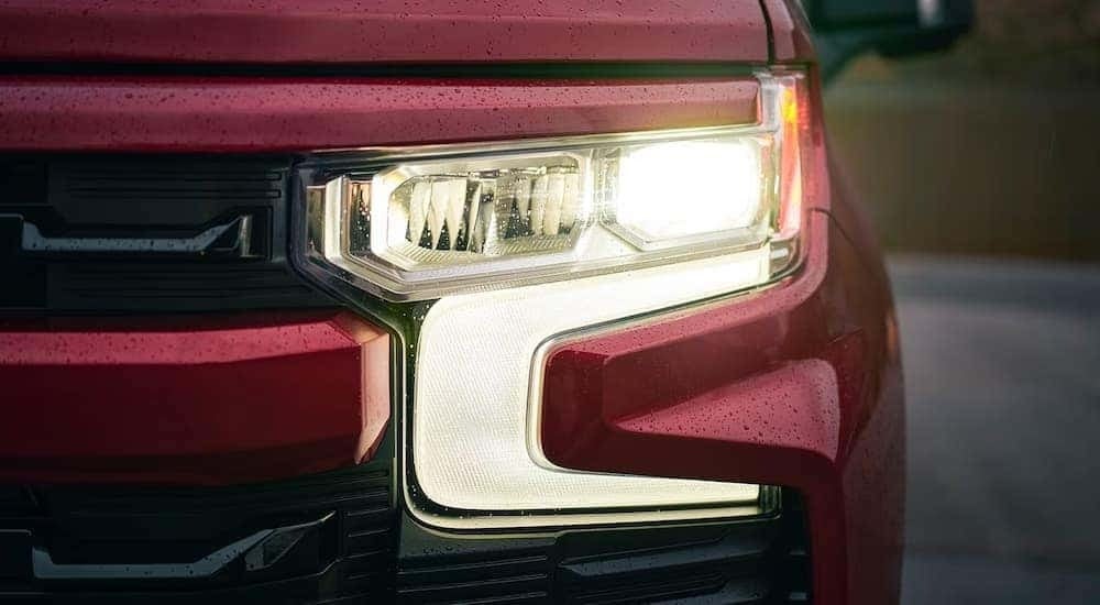 A close up of the front headlight of a red 2024 Chevy Silverado 1500 RST at a Chevy truck dealer.