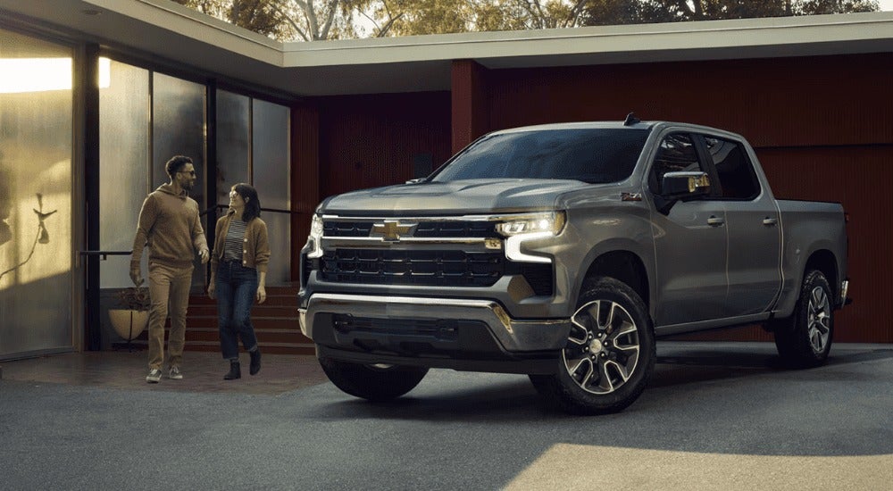 2 people walking towards a silver 2026 Chevy Silverado 1500 for sale.