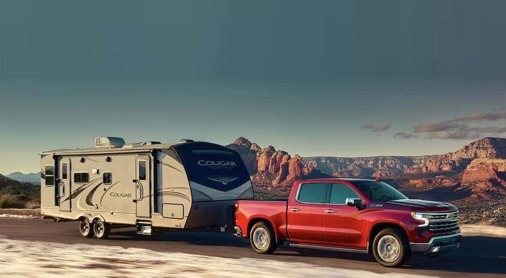 A red 2023 Chevy Silverado 1500 Z71 is shown towing a trailer past distant mountains.