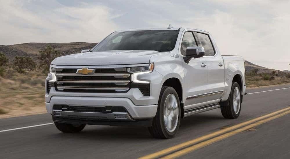 A white 2024 Chevy Silverado 1500 High Country is shown driving on a highway