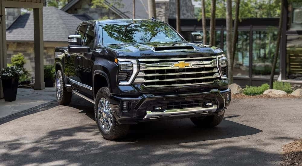 A close up of a black 2024 Chevy Silverado 2500 HD High Country is shown parked in a driveway.
