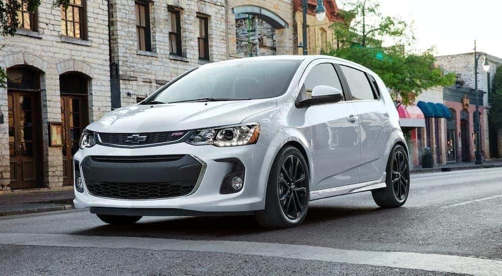 A white 2020 Chevy Sonic RS is shown from the front driving through a city.
