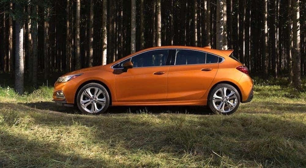 An orange 2018 Chevy Cruze is shown from the side park in front of a row of trees after leaving a used Chevrolet dealer.