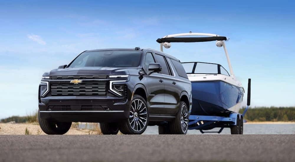 A black 2025 Chevy Suburban is shown from the front at an angle while towing a boat.